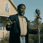 A FROM Season 4 Episode 7 scene showing a character holding a totem outside a yellow house while discussing Boyd’s plan.