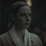 A woman, Juliette in a pale robe stares ahead inside a dimly lit facility in Silo Season 3 Episode 1.
