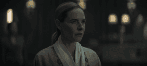A woman, Juliette in a pale robe stares ahead inside a dimly lit facility in Silo Season 3 Episode 1.