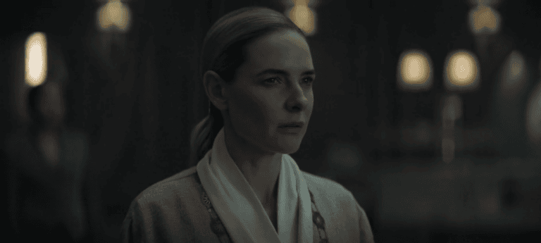 A woman, Juliette in a pale robe stares ahead inside a dimly lit facility in Silo Season 3 Episode 1.