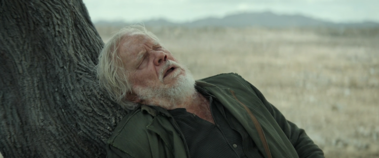 Bernard Holland collapses against a tree after being sent outside to clean without a suit in Silo Season 3 Episode 9.