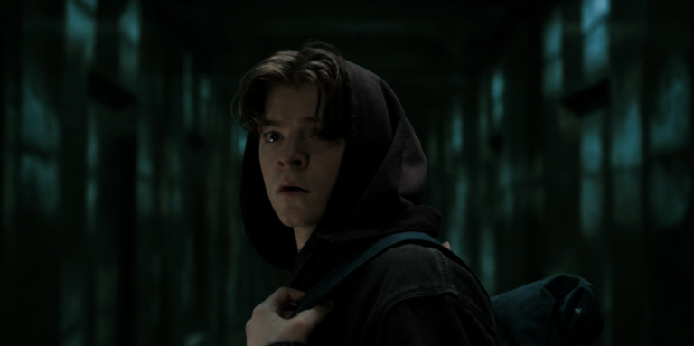 Charlie wearing a dark hoodie and backpack in the Box corridor.