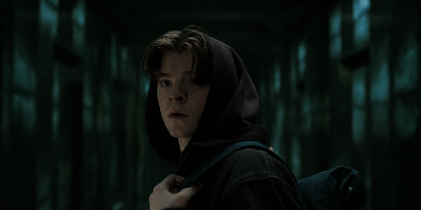 Charlie wearing a dark hoodie and backpack in the Box corridor.
