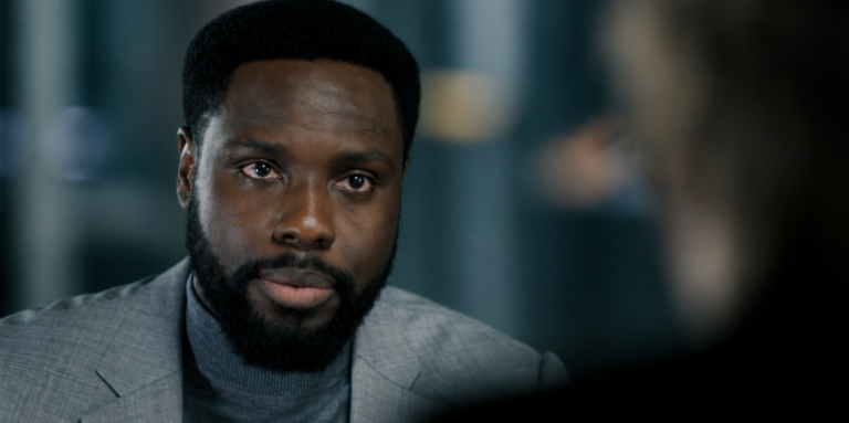 Leighton Vance wearing a gray blazer during a conversation in Dark Matter Season 2 Episode 7.